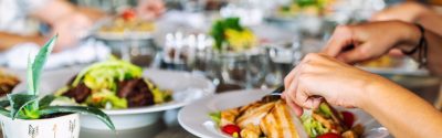 Two hands using a fork and knife to eat their meal with other plates of food in the background