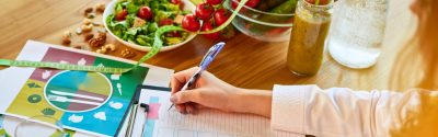 Person filling out a form on a clipboard at a table with a lot of fresh vegetables and other healthy food items