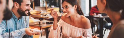 A woman eating food with a fork while her friends talk to her